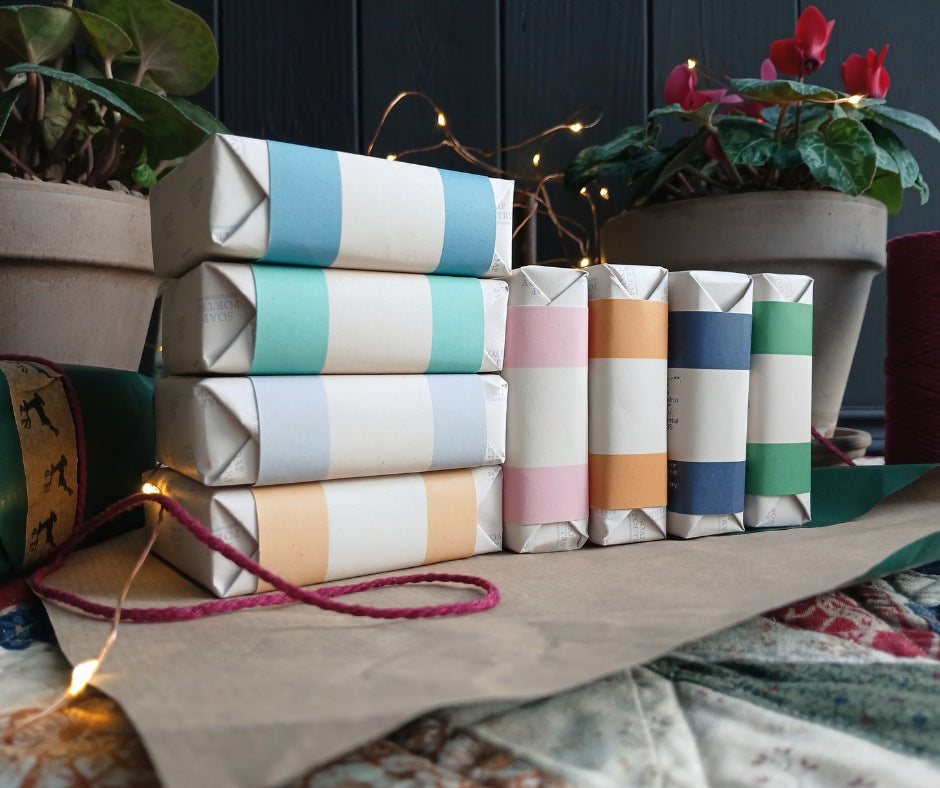 Colorful striped soaps on a quilted tabletop with plants and string lights in the background.