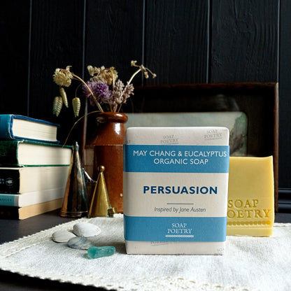 Bar of soap with 'Persuasion' packaging on a surface with books and decorative items.