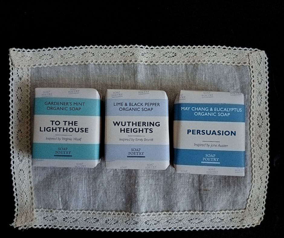 Three bars of soap with literary-themed packaging on a lace-linen table-topper.