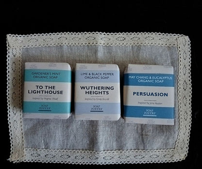 Three bars of soap with literary-themed packaging on a lace-linen table-topper.