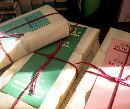 Wrapped soaps with red string and visible branding on a dark wooden background, with the spines of books in the background.