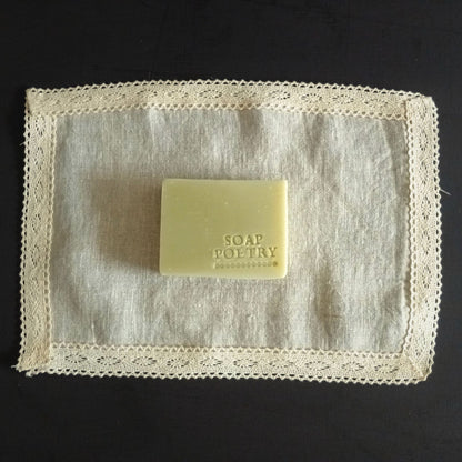 Bar of soap with 'SOAP POETRY' branding stamped into it, on a textured lace-edged linen surface