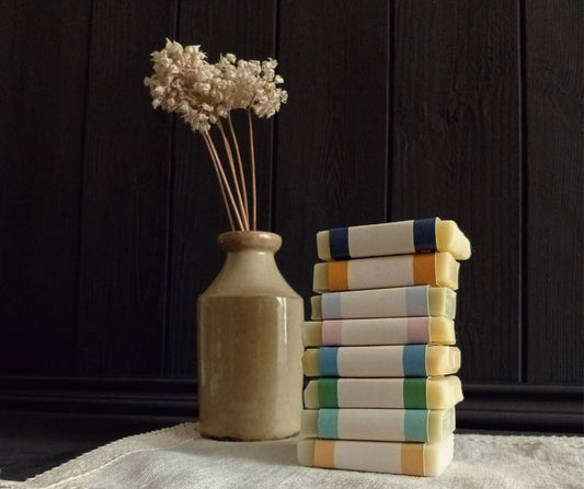 Stack of colorful books next to a vase with dried flowers on a dark wooden surface