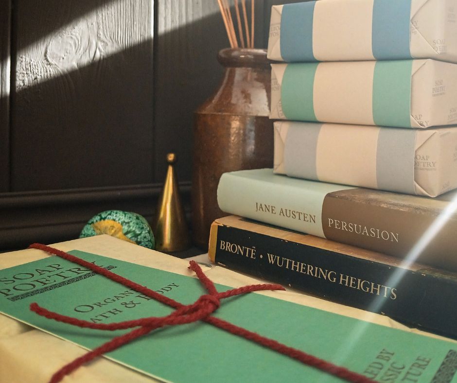 Stack of books with a decorative ribbon on a wooden surface, with a vase and decorative items in the background.