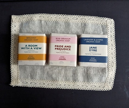 Three organic soap bars with book-themed packaging on a lace doily.
