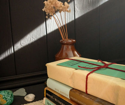 Stack of books with a decorative cover and vase with dried flowers on a dark wooden surface.