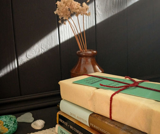 Stack of books with a decorative cover and vase with dried flowers on a dark wooden surface.